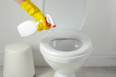 Photo of Woman with spray cleaning toilet seat in bathroom, closeup