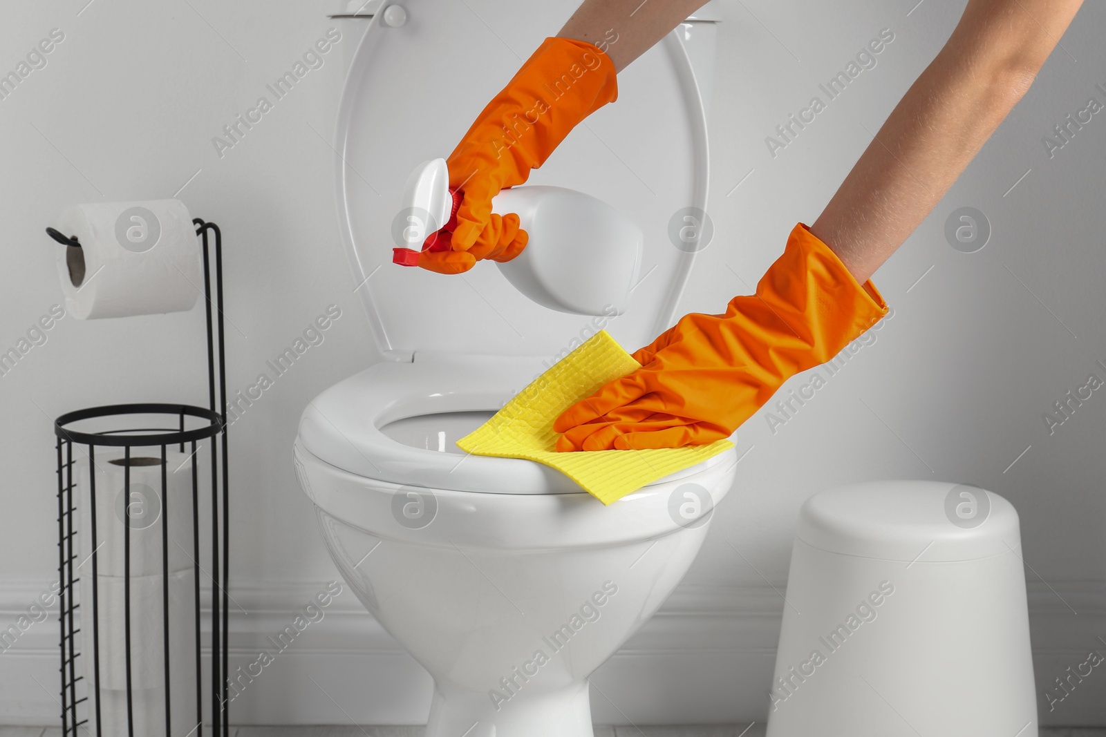 Photo of Woman with spray and rag cleaning toilet seat in bathroom, closeup