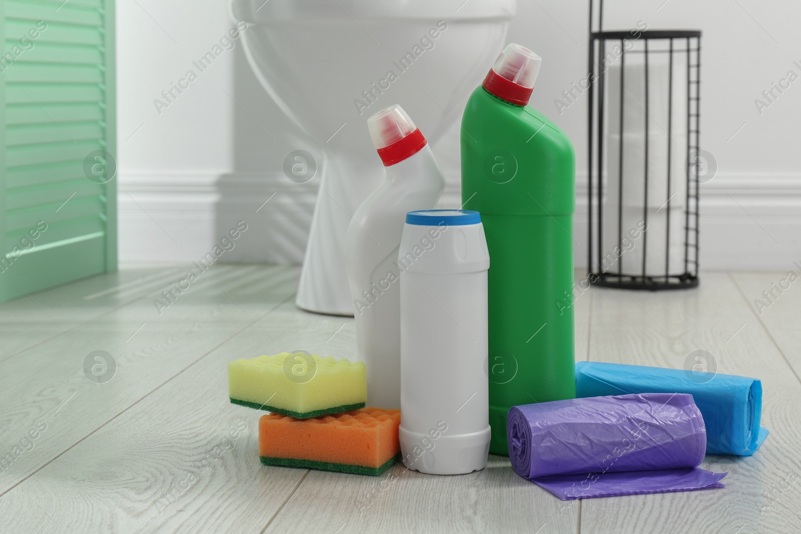 Photo of Toilet cleaners, sponges and trash bags on floor in bathroom, closeup