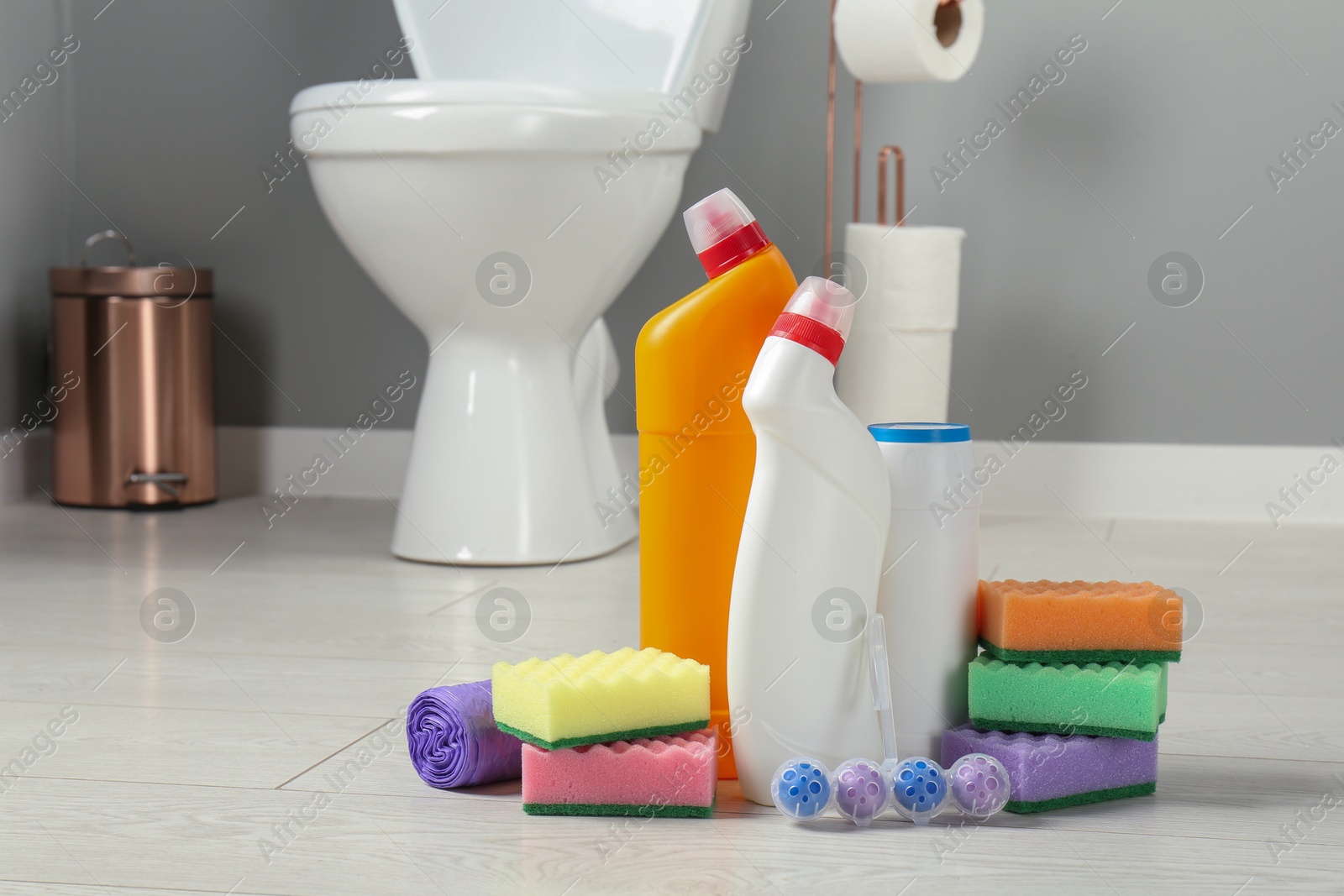 Photo of Toilet cleaners, sponges and trash bags on floor in bathroom, closeup