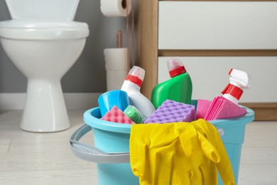 Photo of Bucket with different toilet cleaners, rag, sponge and gloves in bathroom, closeup