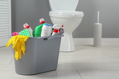 Photo of Bucket with different toilet cleaners, sponge and gloves on floor in bathroom