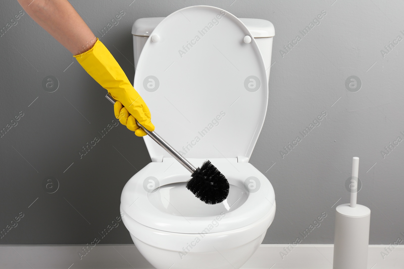 Photo of Woman cleaning toilet with brush in bathroom, closeup