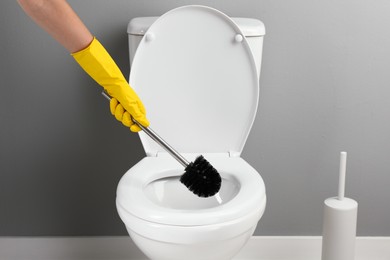 Photo of Woman cleaning toilet with brush in bathroom, closeup