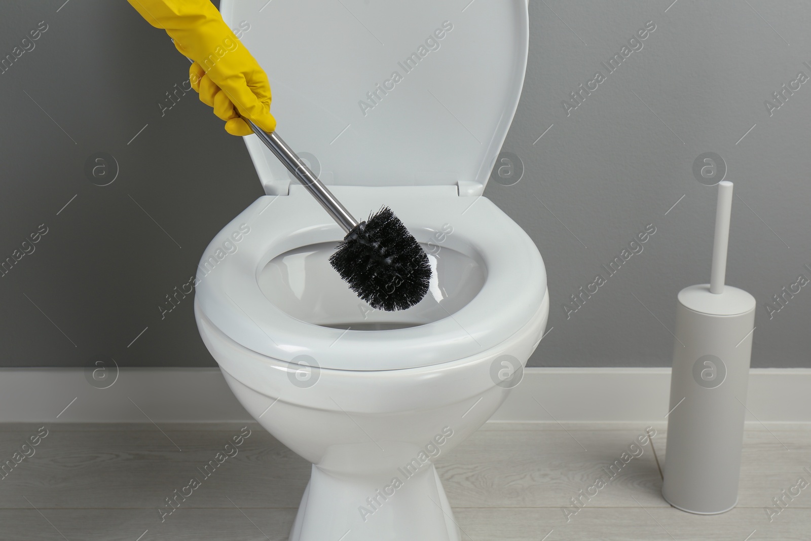 Photo of Woman cleaning toilet with brush in bathroom, closeup