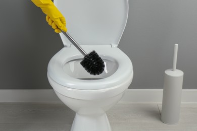 Photo of Woman cleaning toilet with brush in bathroom, closeup