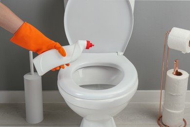 Photo of Woman cleaning toilet with detergent in bathroom, closeup