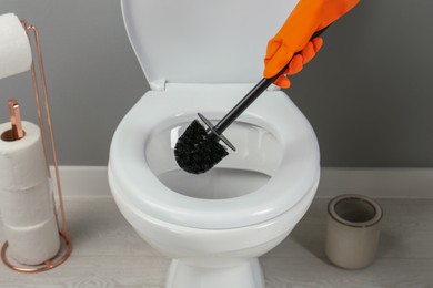 Photo of Woman cleaning toilet with brush in bathroom, closeup