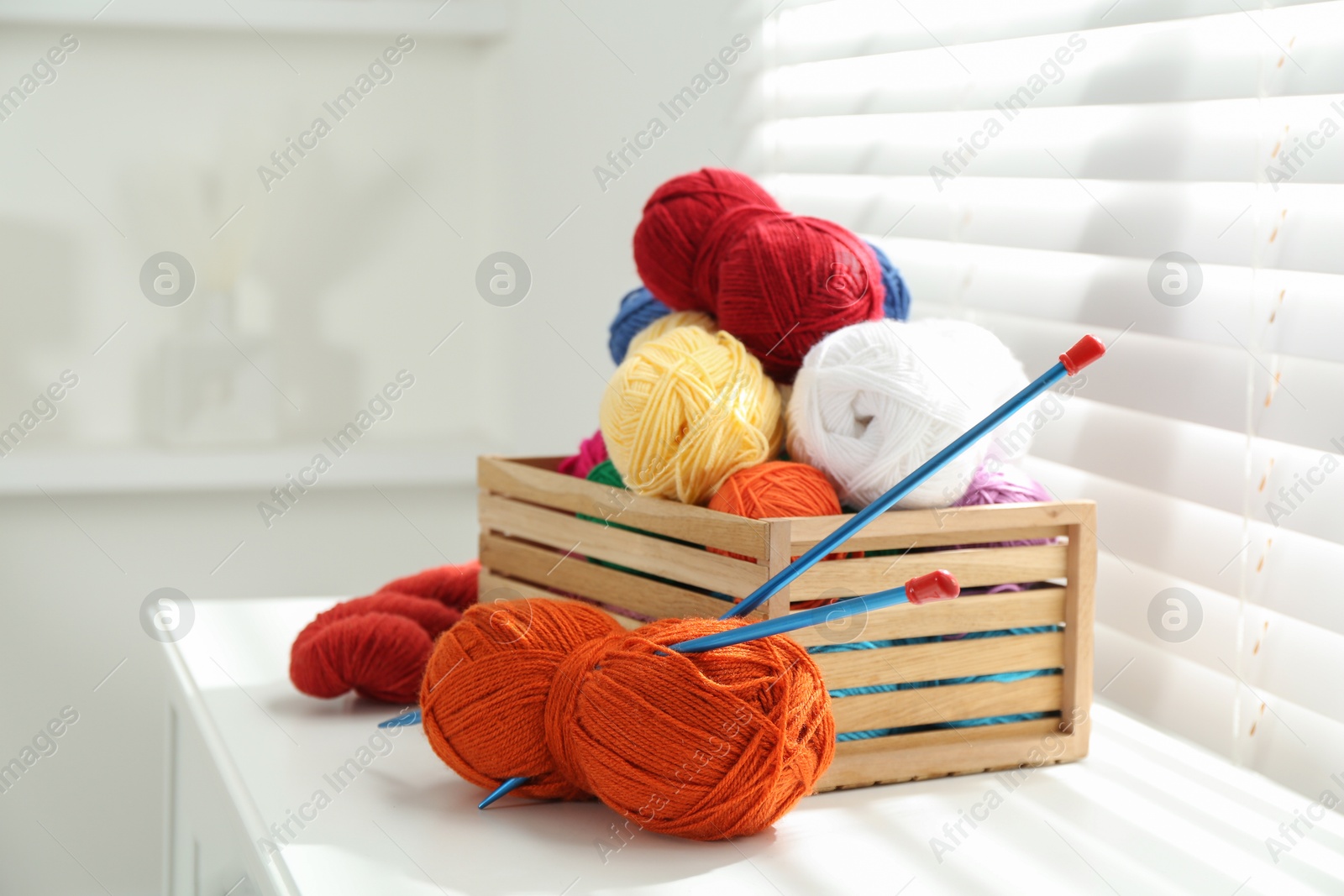 Photo of Soft yarn in crate and knitting needles on chest of drawers indoors