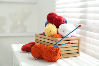 Photo of Soft yarn in crate and knitting needles on chest of drawers indoors