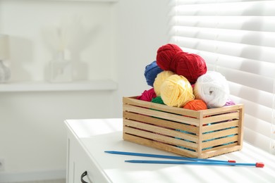 Photo of Soft yarn in crate and knitting needles on chest of drawers indoors