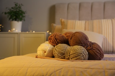 Photo of Skeins of soft yarn and knitting needles on bed indoors