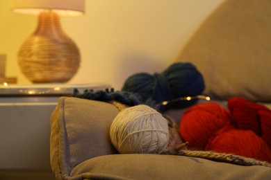 Photo of Knitting material. Skeins of soft yarn and crochet hook on sofa indoors