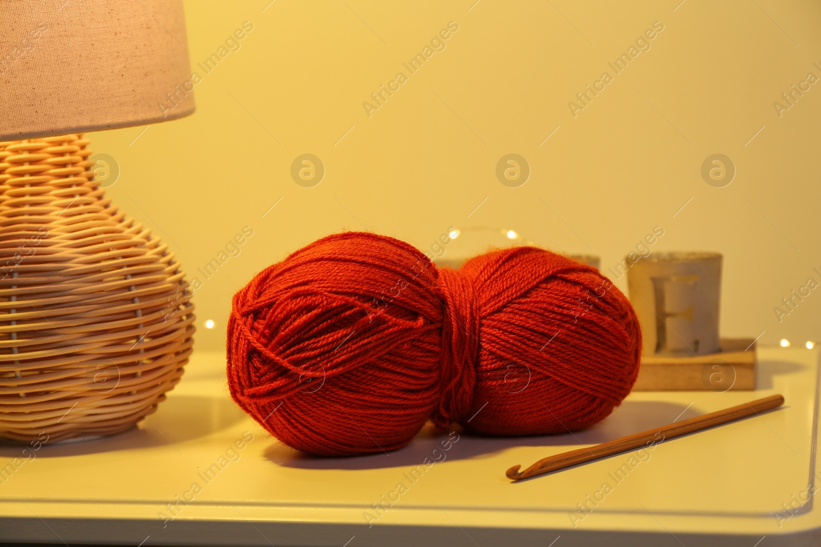 Photo of Knitting material. Skein of soft yarn, crochet hook and lamp on table indoors