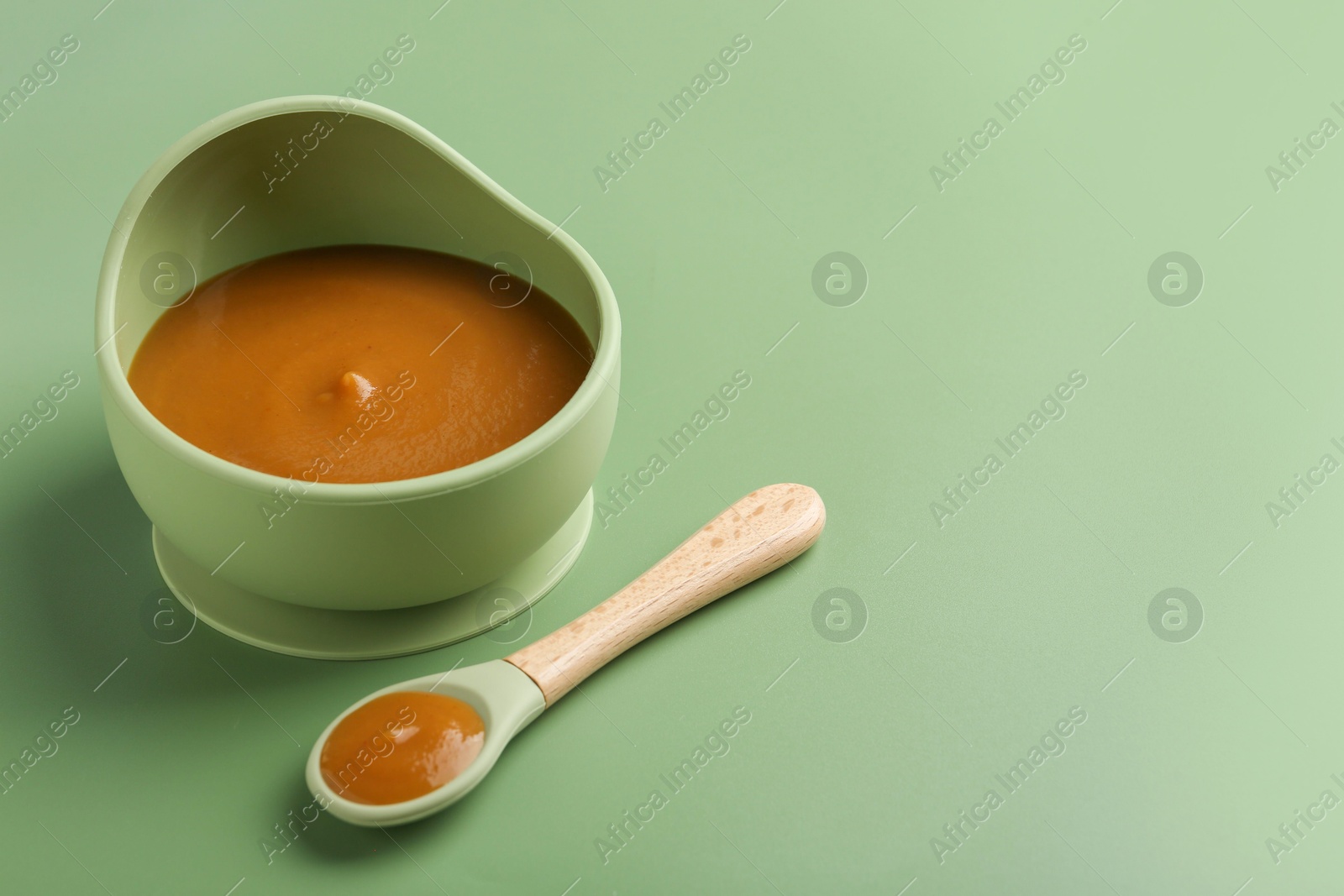 Photo of Delicious baby food in bowl with spoon on green table, space for text