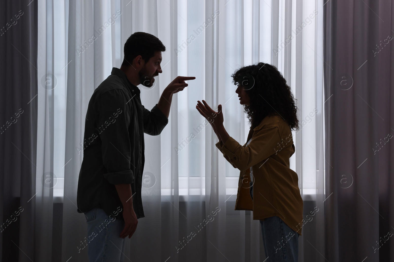 Photo of Emotional couple arguing indoors at night. Relationship problems