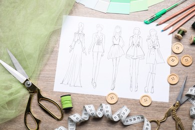 Photo of Sketch of stylish clothes and other fashion designer`s supplies on wooden table, flat lay