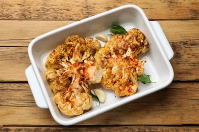 Photo of Tasty cauliflower steaks in baking dish and spices on wooden table, top view