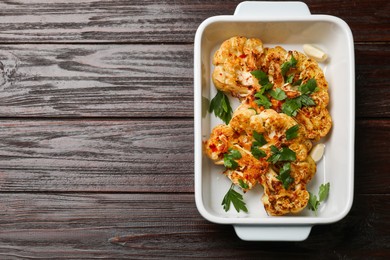 Photo of Tasty cauliflower steaks and parsley in baking dish on wooden table, top view. Space for text