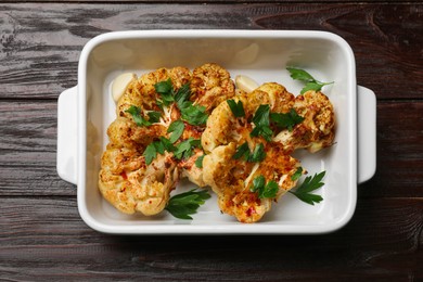 Photo of Tasty cauliflower steaks and parsley in baking dish on wooden table, top view