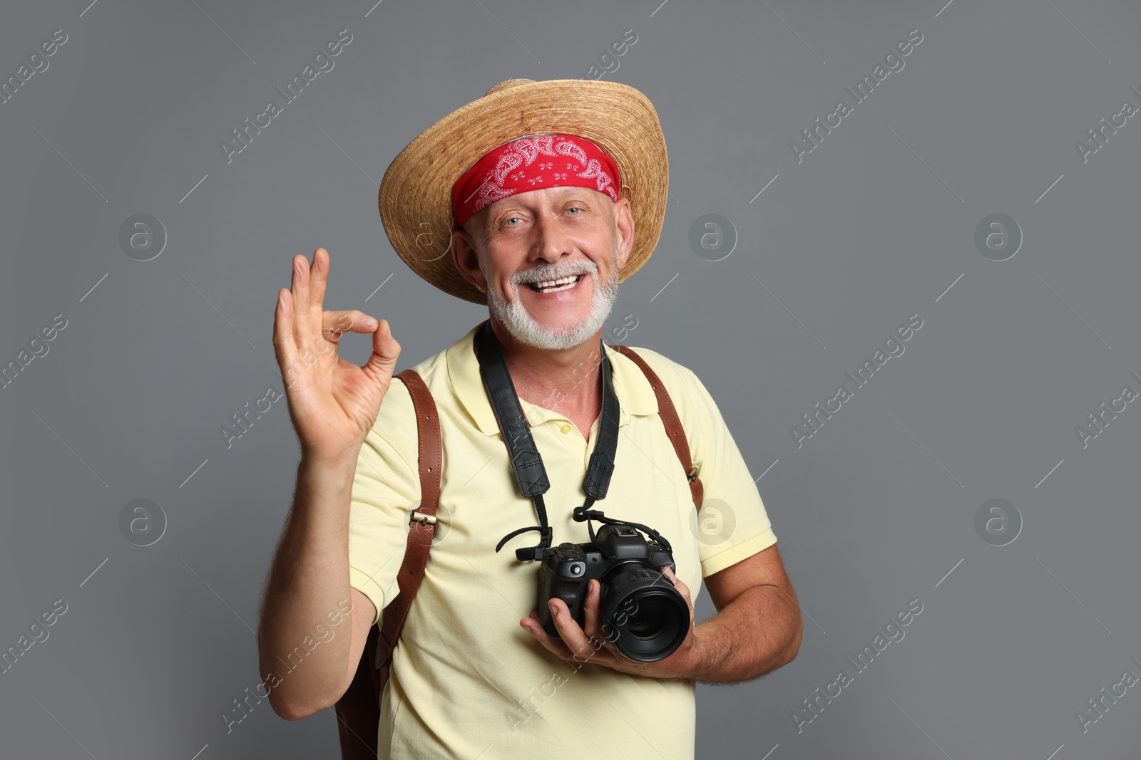 Photo of Portrait of happy senior man with camera showing ok gesture on grey background