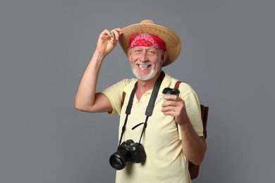 Portrait of happy senior man with camera and paper cup on grey background