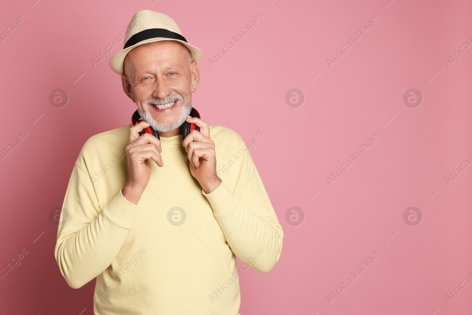 Photo of Portrait of happy senior man with headphones on pink background. Space for text