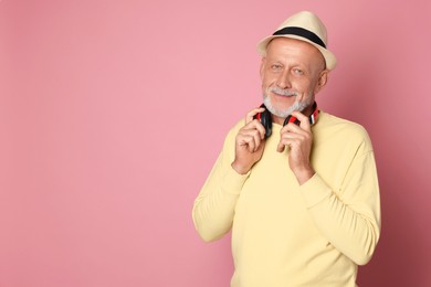 Portrait of handsome senior man with headphones on pink background. Space for text