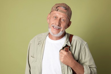 Portrait of happy senior man with backpack on green background