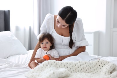 Beautiful young mother and her cute little baby with toy on bed at home