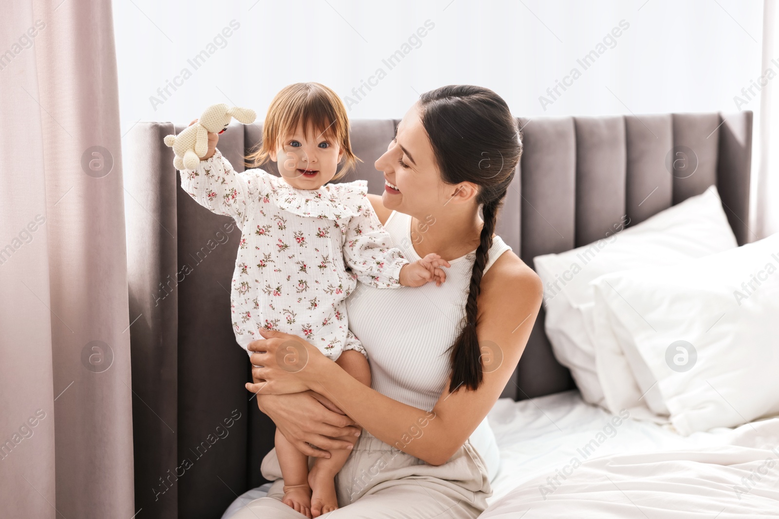 Photo of Beautiful young mother and her cute little baby with rabbit toy on bed at home