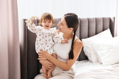 Beautiful young mother and her cute little baby with rabbit toy on bed at home