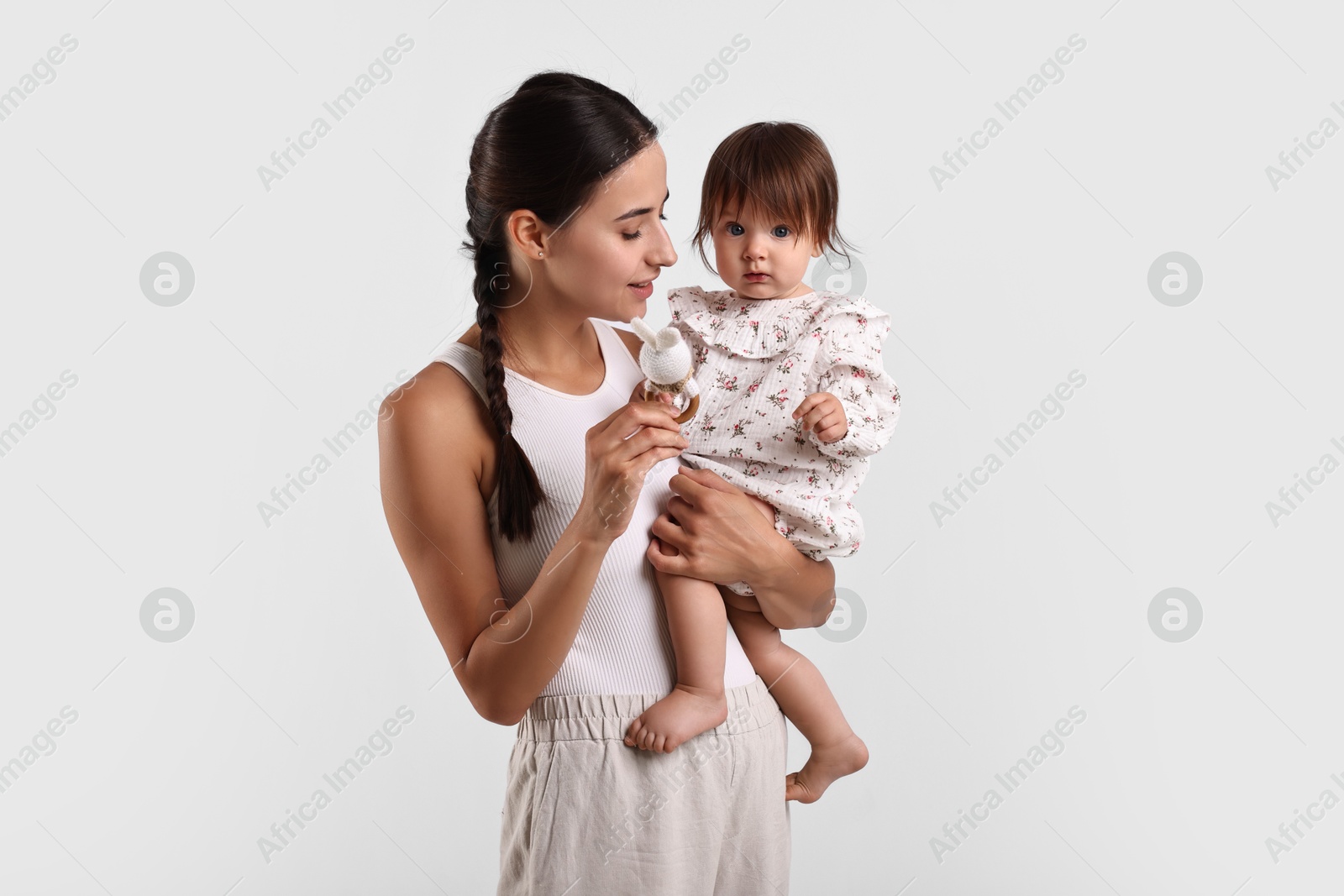 Photo of Beautiful young mother and her cute little baby with rattle on light grey background