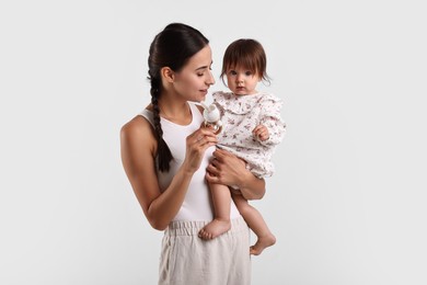 Photo of Beautiful young mother and her cute little baby with rattle on light grey background