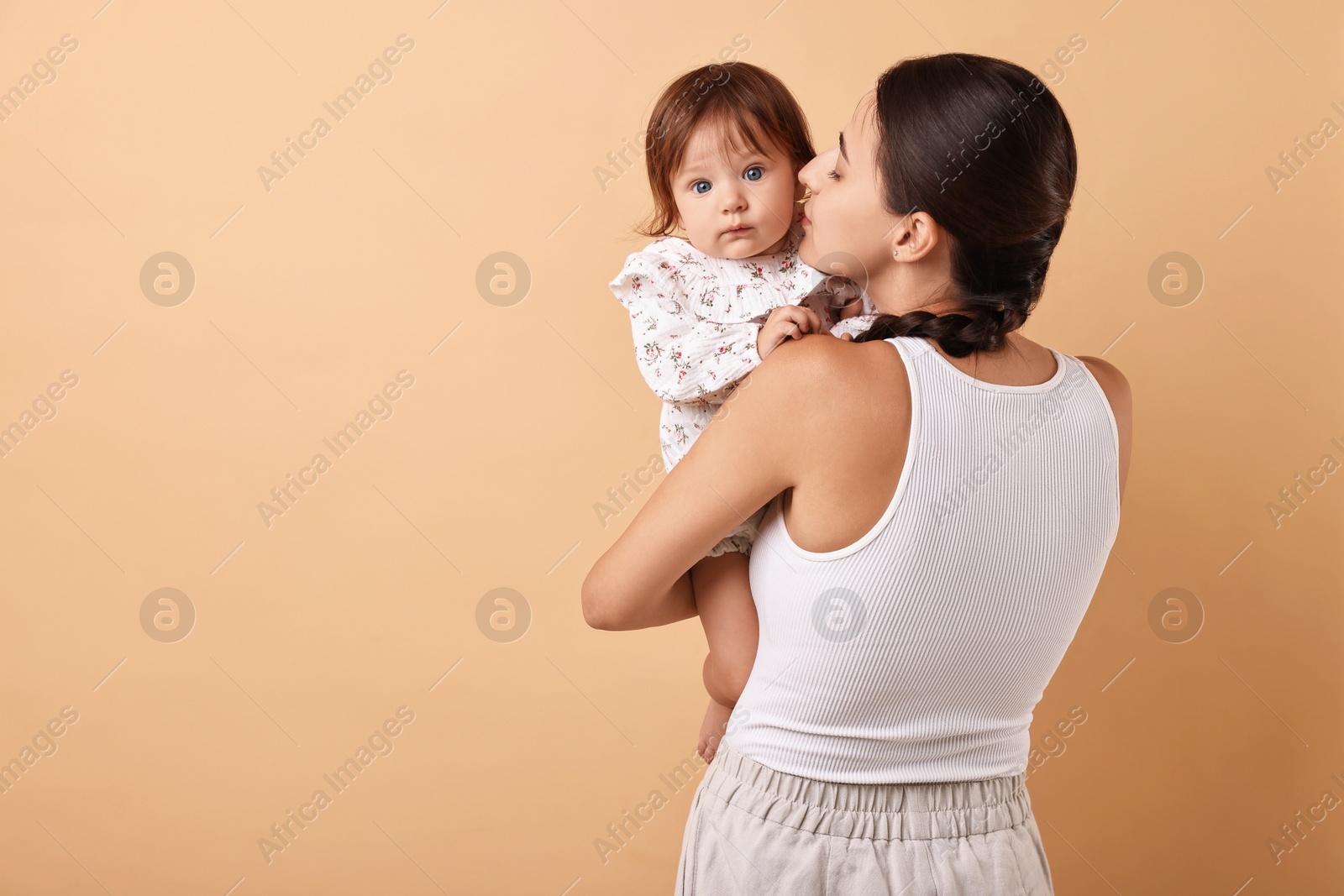 Photo of Beautiful young mother and her cute little baby on beige background, space for text