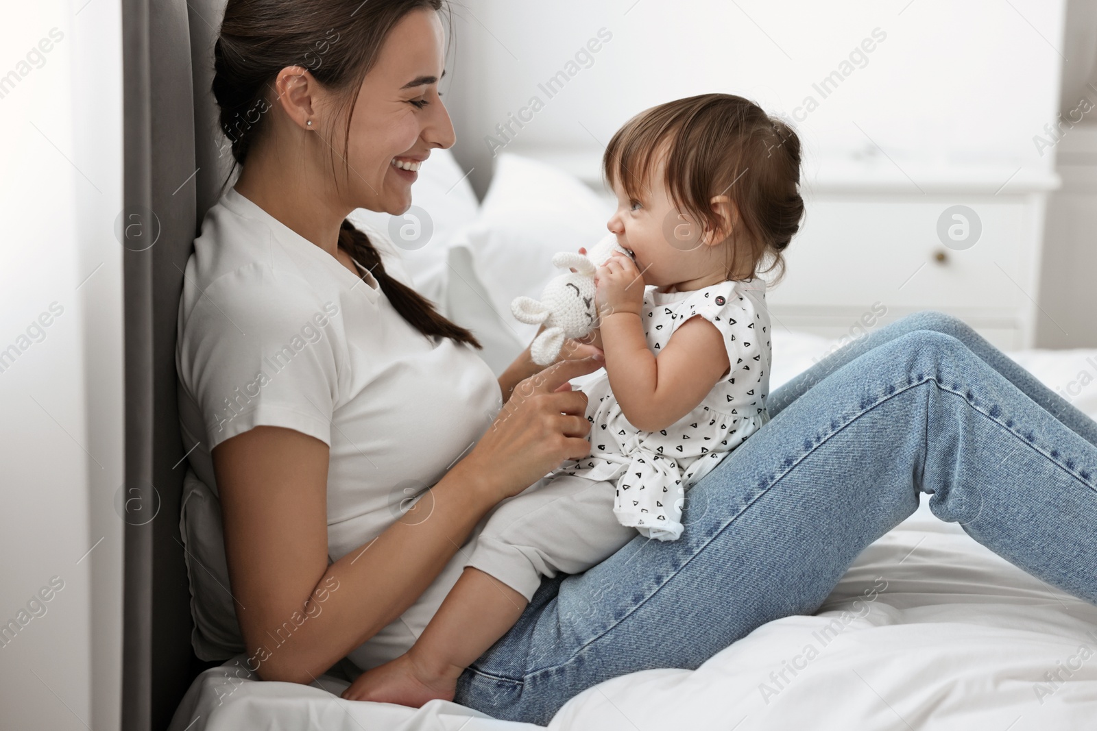 Photo of Beautiful young mother and her cute little baby with rabbit toy on bed at home