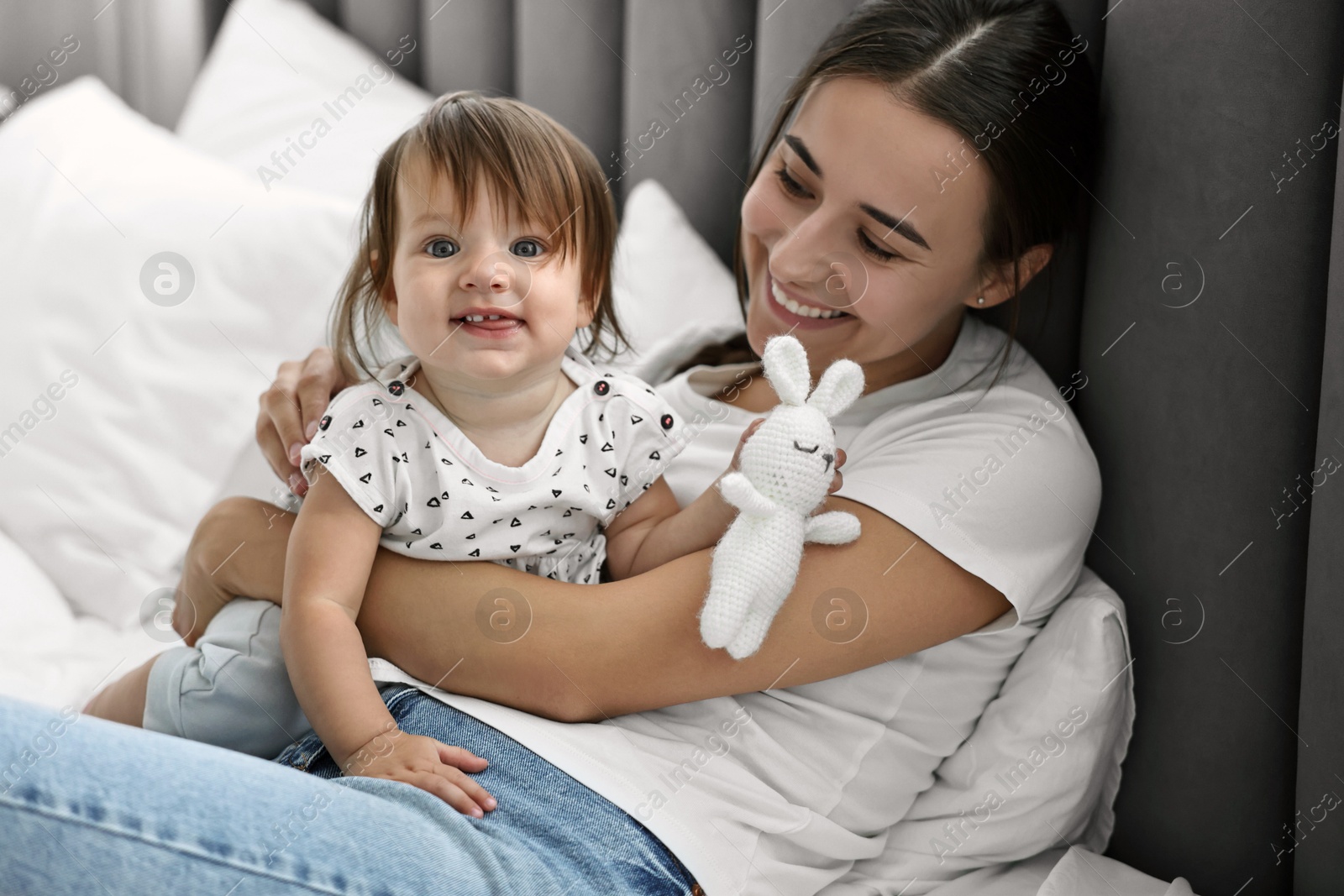 Photo of Beautiful young mother and her cute little baby with rabbit toy on bed at home