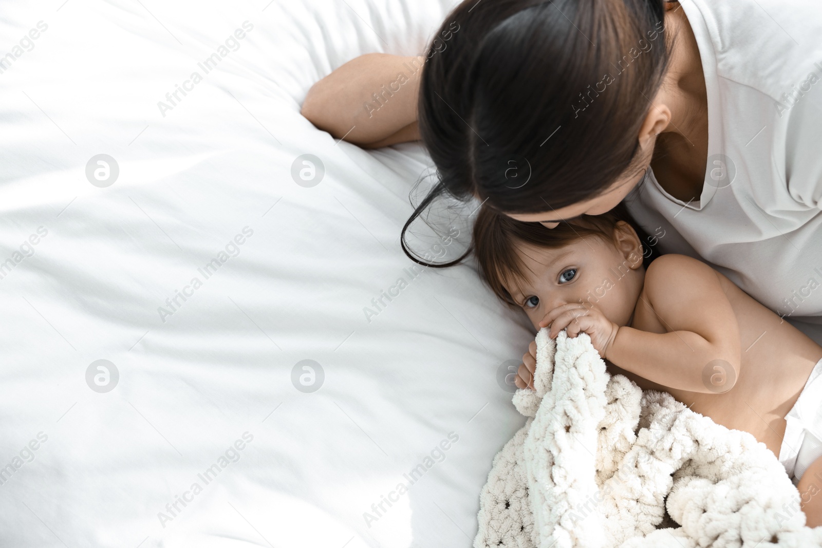 Photo of Young mother with her cute little baby on bed, above view