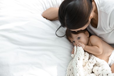 Photo of Young mother with her cute little baby on bed, above view