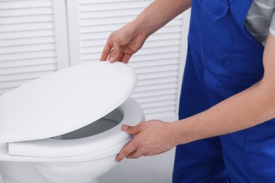 Photo of Man fixing toilet seat in bathroom, closeup