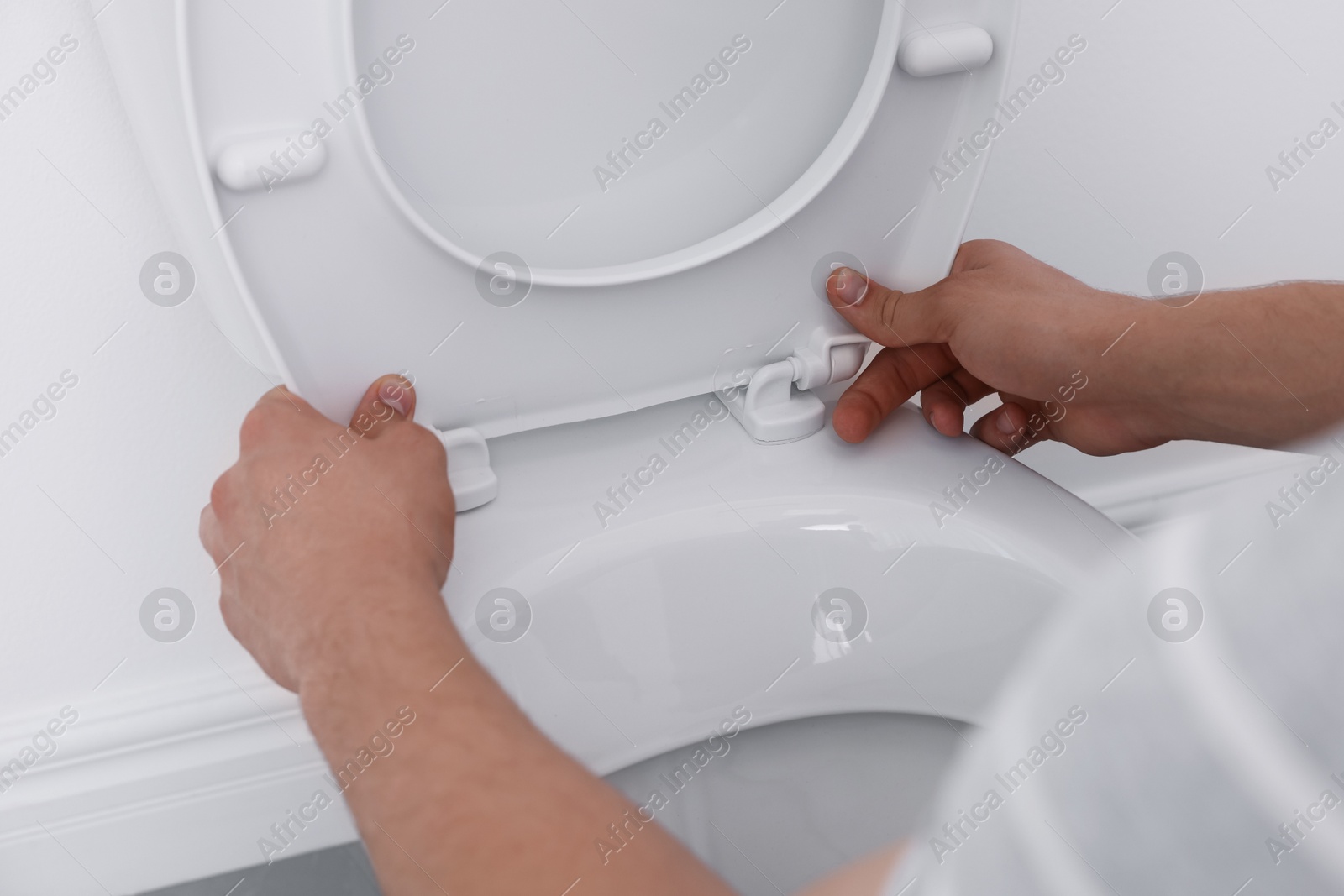 Photo of Man fixing toilet seat in bathroom, closeup