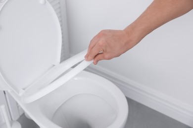 Photo of Man closing toilet seat in bathroom, closeup