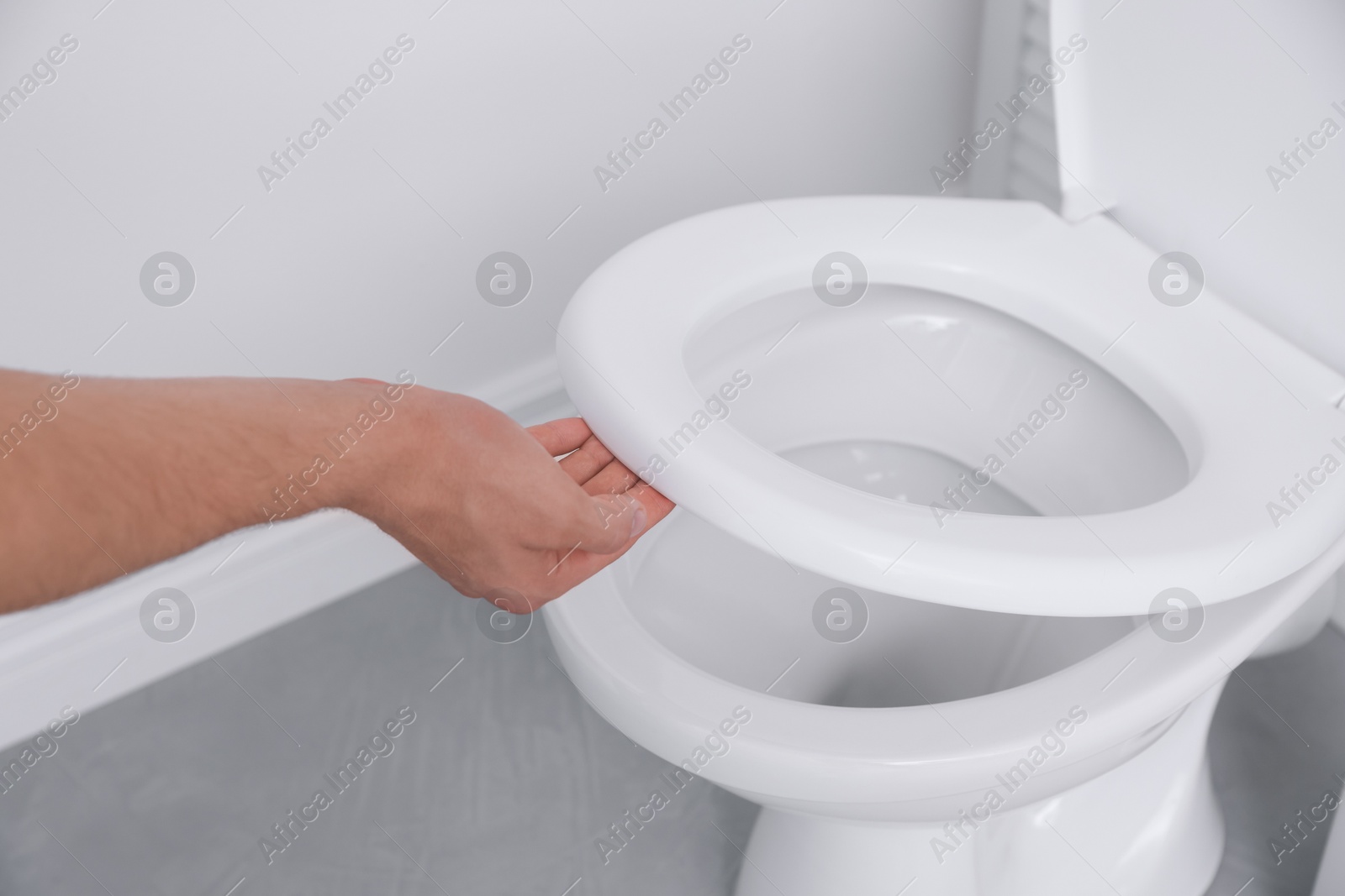 Photo of Man closing toilet seat in bathroom, closeup