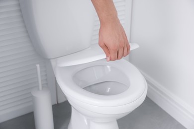 Photo of Man closing toilet seat in bathroom, closeup