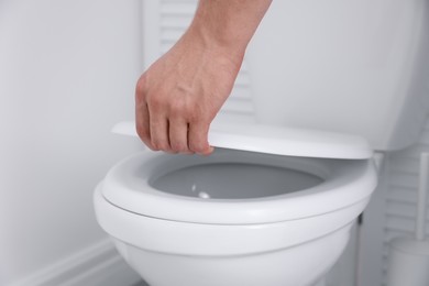 Photo of Man closing toilet seat in bathroom, closeup