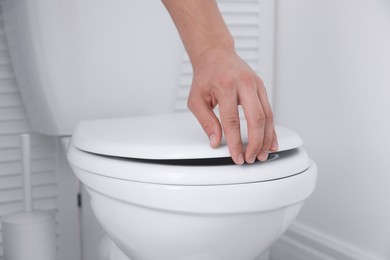 Photo of Man closing toilet seat in bathroom, closeup