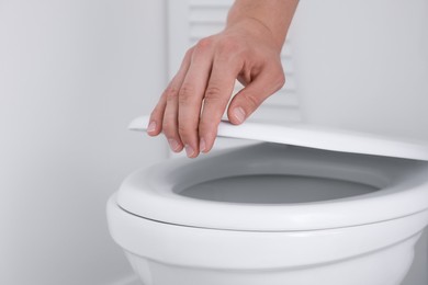 Photo of Man closing toilet seat in bathroom, closeup