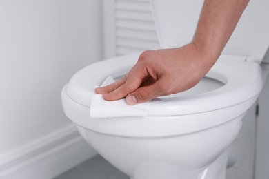 Photo of Man wiping toilet seat with paper in bathroom, closeup