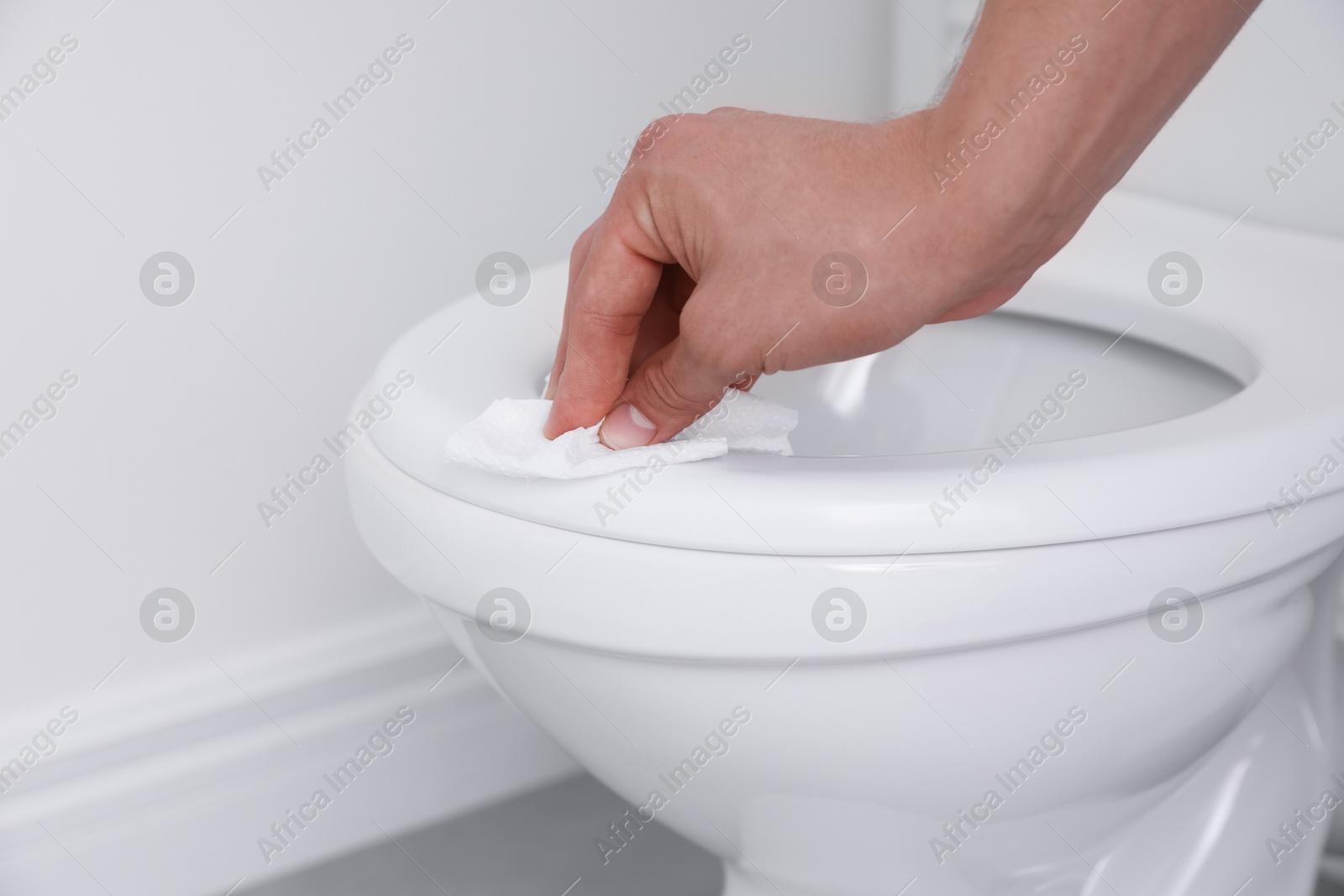 Photo of Man wiping toilet seat with paper in bathroom, closeup