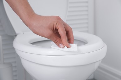 Photo of Man wiping toilet seat with paper in bathroom, closeup